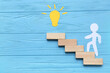 © Pixel-Shot - Paper human figure with light bulb and blocks on blue wooden background. Coaching concept