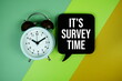 © may1985 - It's Survey Time text on speech bubble with alarm clock top view on green and yellow geometric background