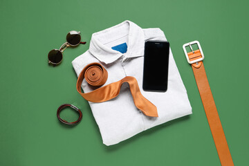 Stylish men's accessories with shirt and modern mobile phone on green background