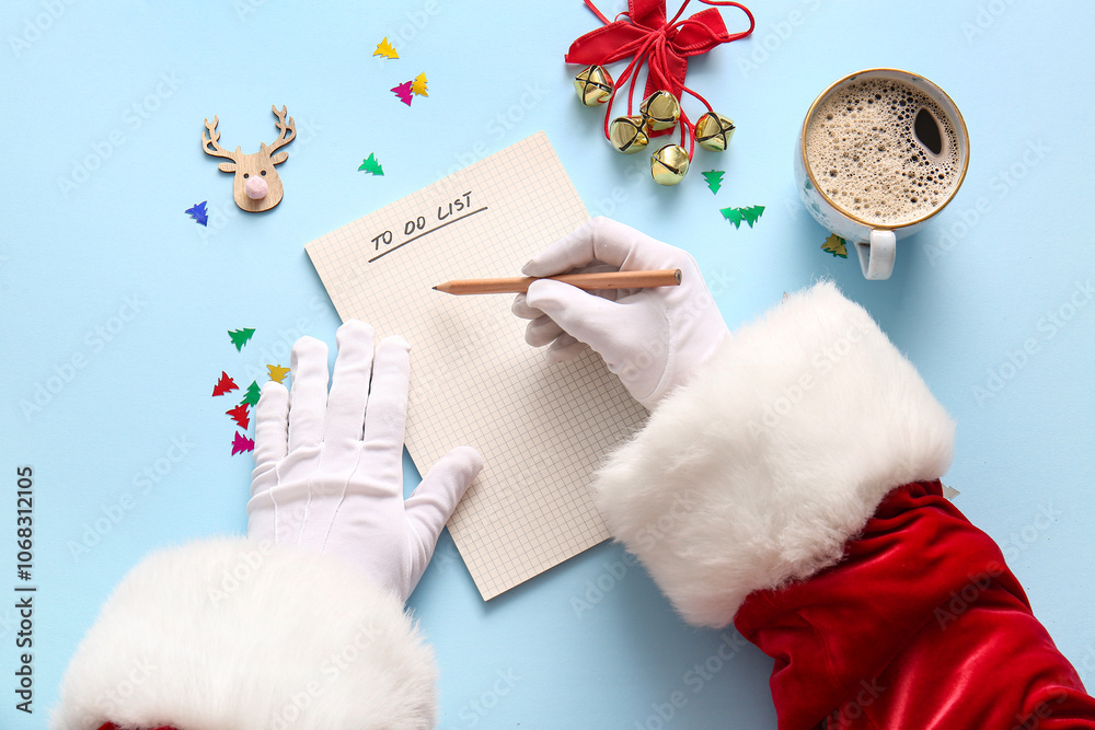 Santa Claus writing to-do list with Christmas decor on blue background
