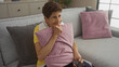© Krakenimages.com - A senior hispanic woman with short hair, in a yellow shirt, holding a remote control and hugging a pink cushion in a cozy living room at home.