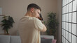 © Krakenimages.com - A young hispanic man holds his teckel dog in a cozy living room, featuring indoor plants, a modern sofa, and large windows, conveying a sense of comfort and companionship at home.