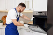 © New Africa - Repairman in uniform examining oven in kitchen