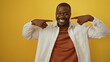 © Krakenimages.com - Young man points to his smile while standing confidently against a vibrant yellow background, showcasing a joyful expression and relaxed demeanor.