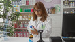 © Krakenimages.com - A middle-aged hispanic woman pharmacist examines a bottle in a well-stocked pharmacy with various products around her.