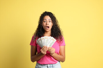 Wall Mural - Shocked woman with dollar banknotes on yellow background