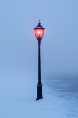 Wall Mural - A street lamp shines bright red against the dense fog, illuminating the snowy path beside a calm waterfront during a tranquil winter evening