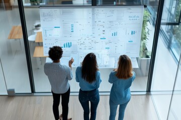 Poster - Three colleagues stand together attentively reviewing a wall of project documents covered with charts and graphs, striving for innovative solutions in a modern workspace.