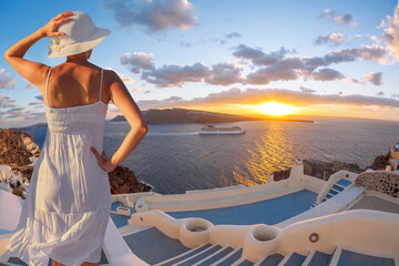 Fototapete - Beautiful young woman enjoying the sunset view of Thira town with tourist boat on Santorini island in Greece