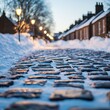 © AucArtStudio - A picturesque cobblestone street lined with snow and charming houses, illuminated by street lamps during twilight.