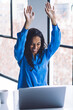 © BullRun - Excited black businesswoman celebrating with hands up in office