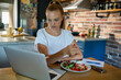 © Geber86 - Woman using laptop on kitchen table while eating healthy meal