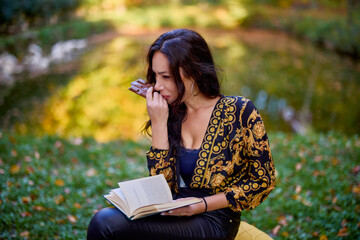 a woman sits by a lake in autumn with a book and eating chocolate