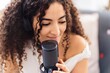 © Studio Marmellata - A close-up of a woman with curly hair and headphones on, as she focuses intently on recording her vocals into a microphone