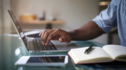 Wall Mural - a man is typing on a laptop in front of a notebook and a cell phone. the laptop is open and the man'