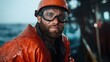 ©  Jovaduplex - A determined worker on a sea voyage dressed in protective orange attire stands on deck, embodying resilience and dedication with waves in the background.
