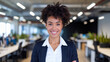 © Tom - A confident young Black woman with natural curly hair smiles proudly in a modern office environment, showcasing her professional demeanor.
