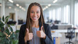 © Tom - A confident young Black woman with braided hair gives a thumbs up in a bright office space, showcasing positivity and professionalism.