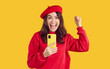 © Studio Romantic - Overjoyed woman expressing her excitement, shouting and clenching fists while holding mobile phone. Joyful emotional woman in sweatshirt and beret holding smartphone, isolated on orange background.