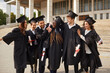 © Studio Romantic - Group of a smiling happy multiracial excited graduates students hugging and having fun in a university graduate gown holding diploma in hands outdoor. Education and graduation concept.