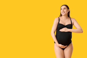 Wall Mural - Young pregnant woman in swimsuit on yellow background. Travel concept