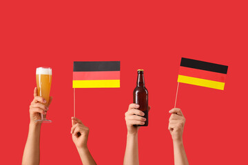 Wall Mural - Male hands with Germany flags, glass and bottle of cold beer on red background. Octoberfest celebration