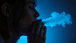 © Irina - Profile of a young woman exhaling vapor against a dark blue background, creating a moody and atmospheric effect, copy space