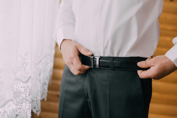 A man is wearing a black belt and adjusting it. Concept of formality and attention to detail, as the man is making sure his belt is properly fastened