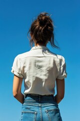 Poster - A woman stands outdoors under a clear blue sky with fluffy white clouds, possibly in a contemplative or peaceful atmosphere