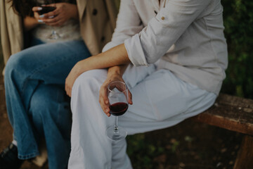 Two friends enjoy a relaxing outdoor moment, seated together with glasses of red wine. The atmosphere is casual and warm, conveying friendship and leisure in a natural setting.