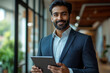 © FATNA - Confident Indian business man leader looking aside walking in office. Busy professional businessman going in hallway holding digital tablet thinking of work plan using tab computer. Authentic photo