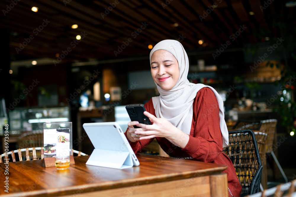 Confident young woman in a cafe uses her smartphone and tablet. She ...