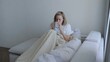 © Alexander - Young woman covered with a warm blanket drinks tea at home. A young woman drinks hot tea while lying on the sofa. A woman on the sofa, covered with a blanket, drinks a hot drink.