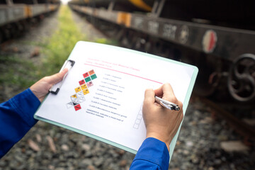 Wall Mural - a worker is checking on chemical hazardous material checklist form with background of train tanker t