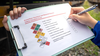 Wall Mural - a worker is checking on chemical hazardous material checklist form with background of train tanker t