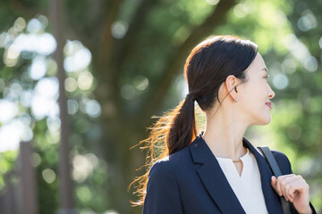 Poster - 逆光の美しい新緑や緑の背景でビジネススーツを着た笑顔の美人な営業マン女性の横顔　見上げるクローズアップのコピースペース　振り返る転職などのイメージ