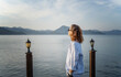 © olezzo - Young woman standing on the pier in the morning admiring the sea and mountain landscape