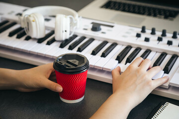 A cup of coffee in the hands of a female keyboard player at the workplace.