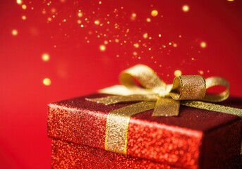 Wall Mural - shiny red gift box with golden ribbon and falling glitter creates festive atmosphere