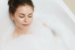 © SHOTPRIME STUDIO - Relaxed young woman enjoying a bubble bath at home, eyes closed with a serene expression, creating a peaceful atmosphere within a modern bathroom setting.