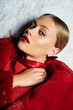 © LIGHTFIELD STUDIOS - A young woman adorned in a vibrant red coat gazes thoughtfully while lying on a snowy background