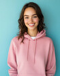 © EmmaStock - A young woman in a casual hoodie, smiling confidently in front of a pastel blue backdrop.