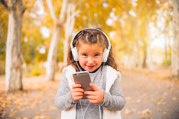 Smiling girl with headphones, enjoying music in a picturesque autumn park setting.