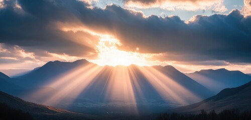 Wall Mural - A dramatic landscape featuring mountains backlit by a setting sun, with rays of light breaking through clouds, creating a sense of awe and depth.