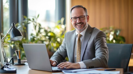 Poster - A smiling man in a suit working on a laptop in a bright, plant-filled office.
