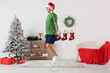 © Pixel-Shot - Young happy man in Santa hat training with skipping rope in living room decorated for Christmas
