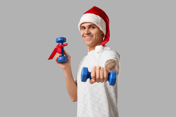 Sticker - Young man in Santa hat holding gift dumbbells on grey background