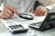 © Yuliia - close-up shot of a young businessman carefully inspecting an invoice with a magnifying glass and calculator on his desk.