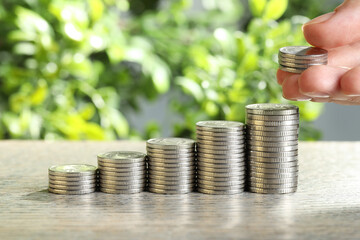 Salary concept. Woman putting coins on stack at grey table, closeup