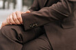 © dikushin - Closeup cropped shot of successful businessman in suit sitting on bench, holding hands on knee outside. Closeup of confident businessman in stylish business attire sitting, holding knee outdoors.
